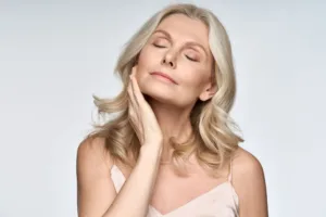 A middle-aged woman with clear skin holding her face.