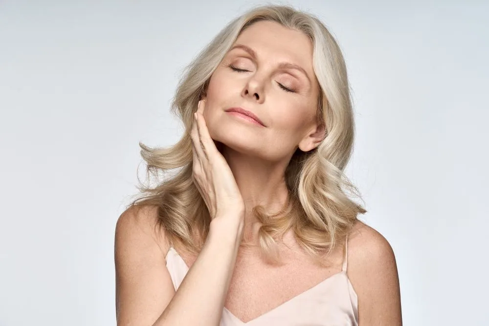 A middle-aged woman with clear skin holding her face.
