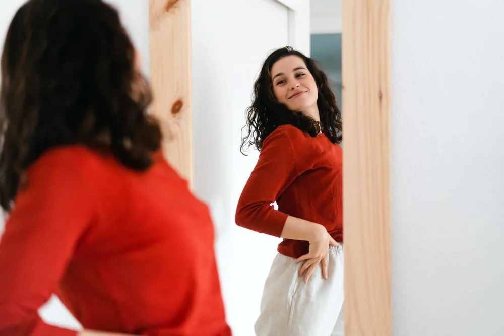 A woman standing in front of the mirror, feeling confident and happy.