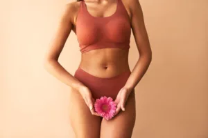 A woman holding up a pink flower on a beige background.