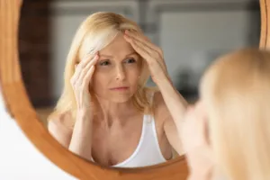 A woman looking into a mirror while struggling with a headache.