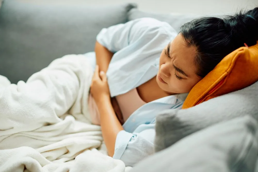 A woman laying on a couch and holding her abdomen in pain.