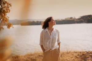 A woman standing near a lake feeling relaxed and confident.