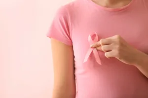 Woman with pink breast cancer ribbon on color background.