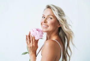 Blonde young woman with pink peony in hand isolated on white background
